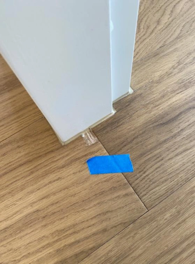 Blue tape on wood floor by wall corner.